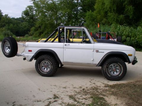 1967 Ford Bronco - A white first-generation Ford Bronco, possibly a 1967 model, is shown with a roll cage and an external spare tire mounted on the rear.