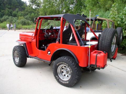 1967 Ford Bronco - A red jeep is parked outdoors with a wooded area in the background and another vehicle behind it.