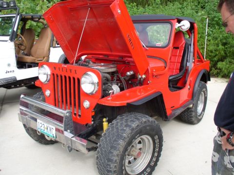 1967 Ford Bronco - A red Willys Jeep is parked next to a white Jeep, with the red Jeep's hood open.