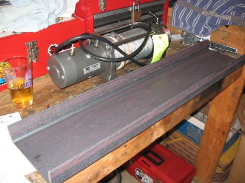 1995 Ford Bronco - A winch and metal channel are on a workbench, with a glass of beer and toolboxes nearby.