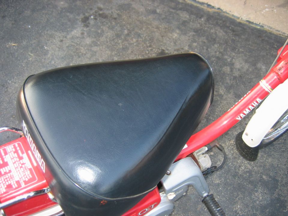 Black moped seat with red frame and white fender. Text 'YAMAHA' visible on frame