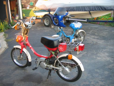 1985 Ford LTD Crown Victoria - Two mopeds are parked in a driveway, with a boat on a trailer in the background.