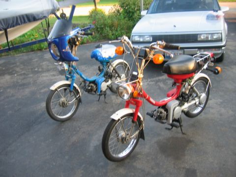1985 Ford LTD Crown Victoria - Two mopeds are parked on asphalt in front of a white car.