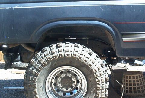 1986 Ford Bronco - The rear wheel well and tire of a modified SUV are shown, with visible suspension components.