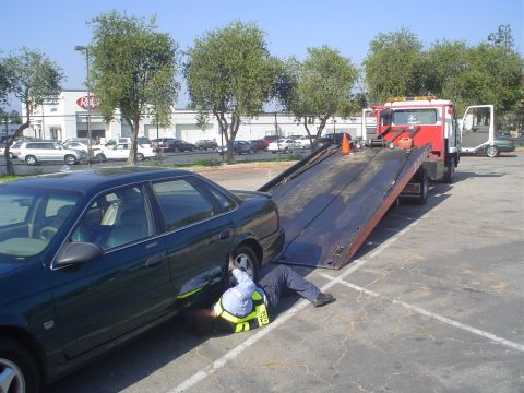 1993 Ford Taurus - A tow truck operator works on a dark green sedan as it is loaded onto the flatbed.