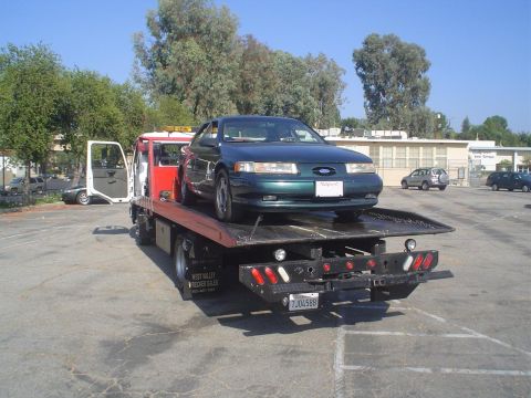 1993 Ford Taurus - A dark green 1993 Ford Taurus is loaded onto a red tow truck, ready to be transported.