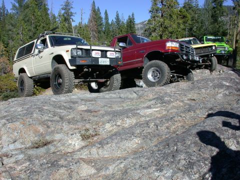 1996 Ford Bronco - Multiple lifted trucks navigate a rocky trail during an off-road excursion.