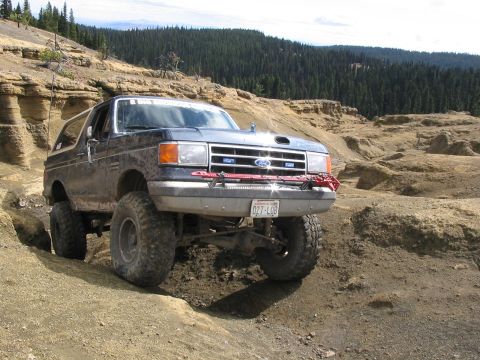 1995 Ford Bronco - A modified Ford Bronco navigates a challenging off-road terrain with steep inclines and rocky formations.
