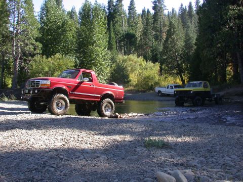 1996 Ford Bronco - A lifted red Ford Bronco is parked by a river with other vehicles in the background.