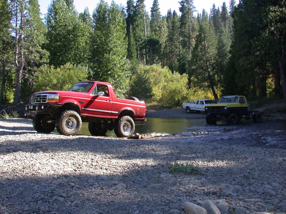 Red Ford Bronco with lifted suspension and off-road tires parked on a rocky shore
