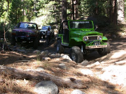 1996 Ford Bronco - A green off-road vehicle navigates a rocky trail, with other vehicles visible in the background.
