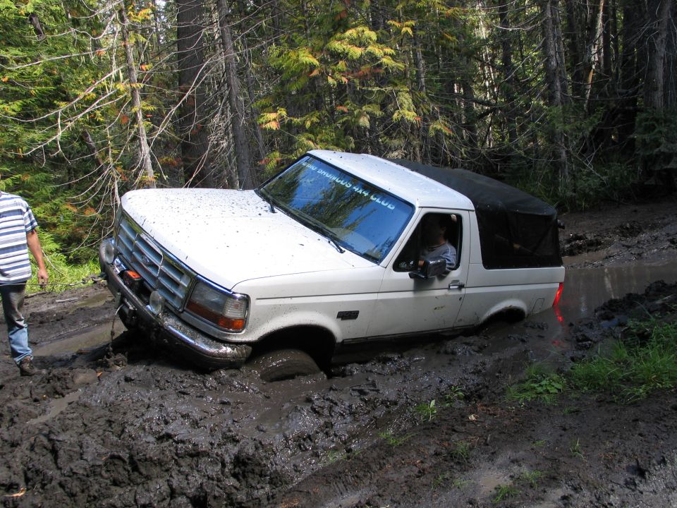 White Ford Bronco stuck in deep mud on a forest trail