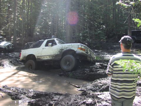 1995 Ford Bronco - A white 1992 Ford Bronco struggles through a muddy off-road trail, with another vehicle visible in the background.