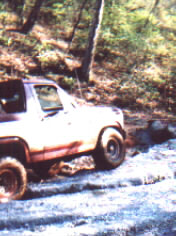 1981 Ford Bronco - This vehicle is navigating a rough, wet terrain with trees in the background.