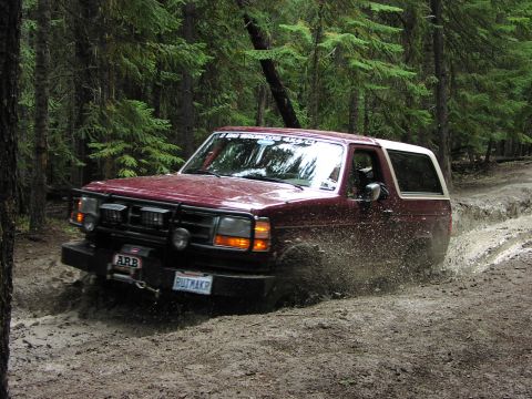 1995 Ford Bronco - A maroon 1995 Ford Bronco navigates a muddy path through a dense forest.