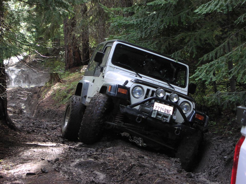 White Jeep Wrangler on muddy forest trail with winch and off-road tires