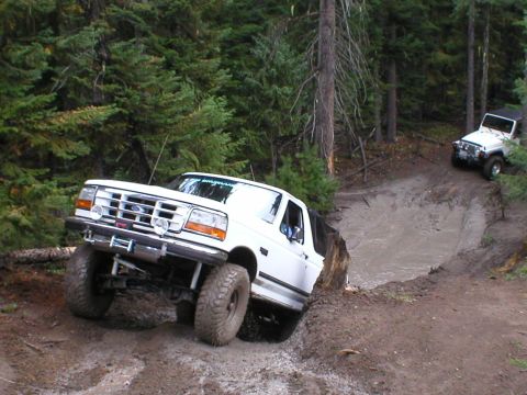 1995 Ford Bronco - Two off-road vehicles, a Ford Bronco and a Jeep, tackle a challenging muddy trail.
