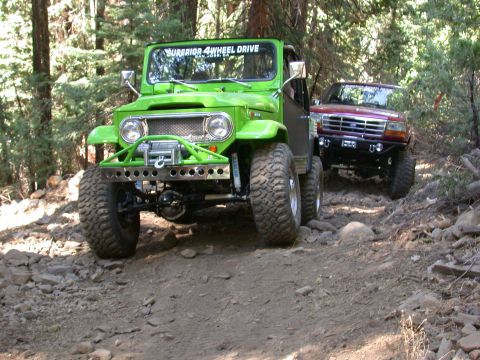 1996 Ford Bronco - Two off-road vehicles navigate a rocky trail in a wooded area.