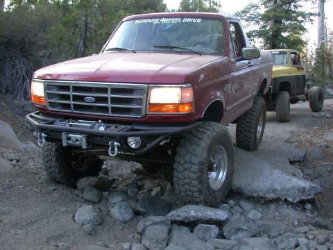 1996 Ford Bronco - A lifted 1996 Ford Bronco navigates a rocky trail, followed by another vehicle.