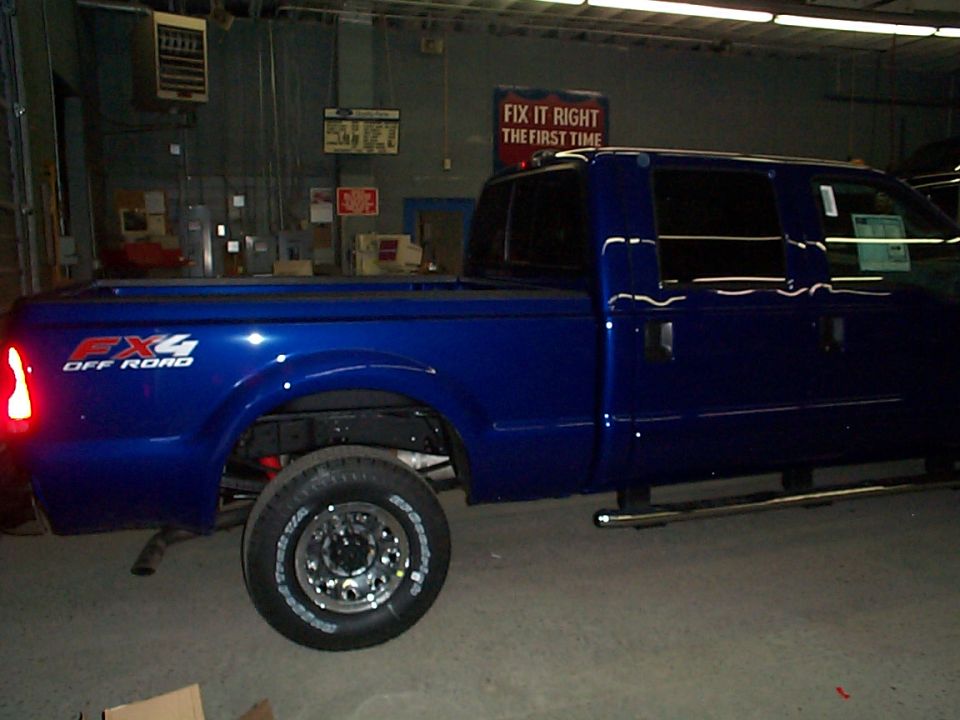 Blue Ford Super Duty crew cab in shop with rear wheel removed, FX4 Off Road decal on bedside