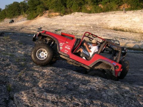 1999 Jeep TJ - A red 1999 Jeep TJ navigates a rocky terrain, demonstrating its off-road capabilities.