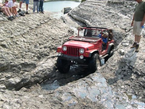 1999 Jeep TJ - A red Jeep Wrangler tackles a challenging off-road course with spectators observing from the side.