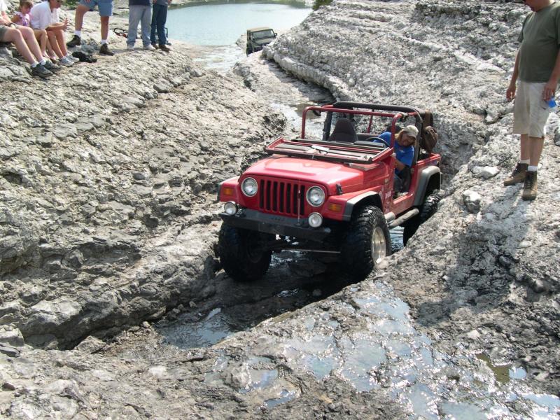 Red Jeep Wrangler TJ with top and doors off crawling down a rocky ledge into mud