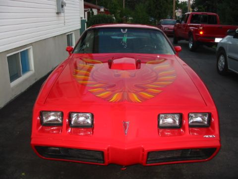 1985 Ford Bronco - A red 1981 Pontiac Firebird Trans Am is parked in front of a building, with other vehicles visible in the background.