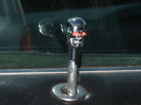 1985 Ford Bronco - A custom skull-shaped door lock knob with red eyes is installed on a vehicle's interior door panel.