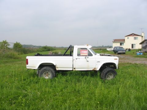 1985 Ford Bronco - Modified white pickup truck sits in a grassy field with a 'A VENDRE' sign in the window.