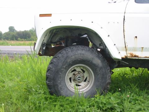 1985 Ford Bronco - Close-up of a white SUV's side, showing its large tires and signs of wear and tear.