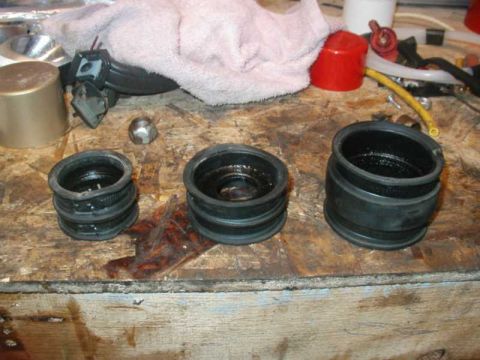 1993 Ford Taurus - Three rubber intake boots and a nut are laid out on a workbench.