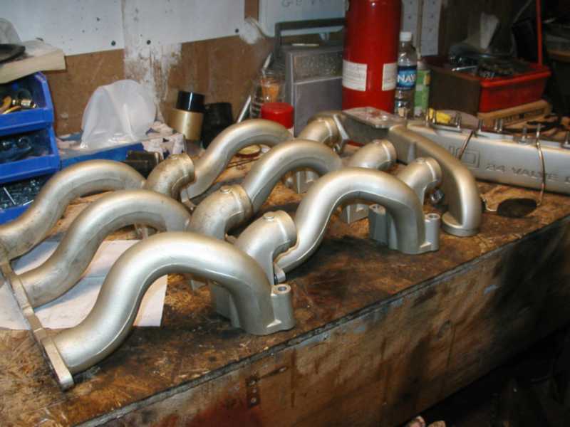 Silver exhaust manifolds on a wooden workbench with tools and a red fire extinguisher in the background