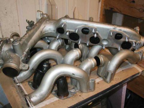 1993 Ford Taurus - A silver intake manifold with several curved pipes and circular ports is shown, resting on a cardboard surface.