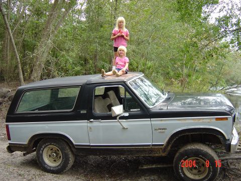 1982 Ford Bronco - A two-tone gray and black Ford Bronco is parked outdoors with two young girls sitting on its roof.