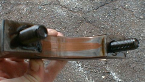1990 Ford Bronco - A worn engine bearing is held for inspection, showing signs of damage and a protruding bolt.