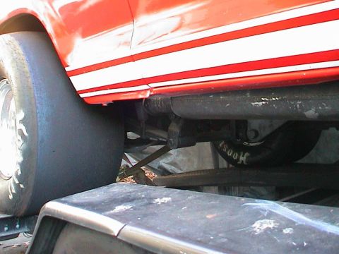 1979 Ford Bronco - Close-up of a red vehicle's side, revealing racing stripes and a large tire, with visible undercarriage components.
