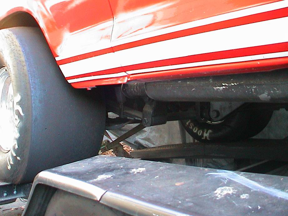 Rear of red striped drag vehicle showing wide Hoosier slick and rear axle and links underneath