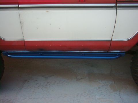 1978 Ford Bronco - Blue rock sliders are mounted to the lower body panel of a two-tone red and white vehicle.