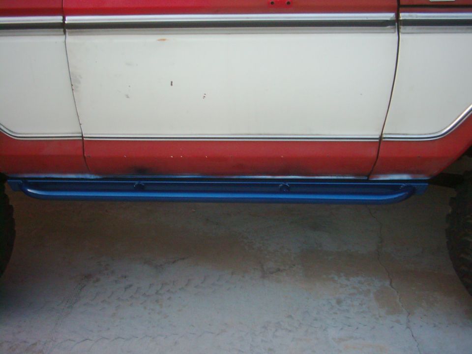 Side view of blue rock sliders installed below the red and white body of a vehicle
