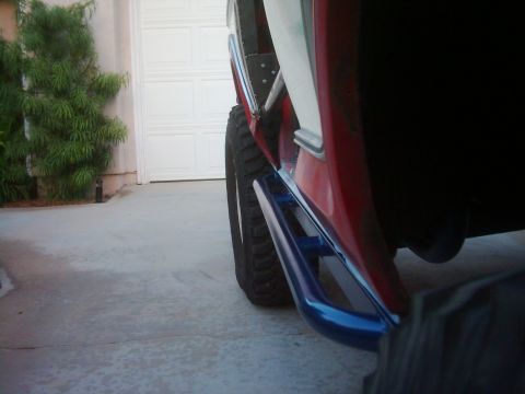 1978 Ford Bronco - Blue rock sliders are visible on the side of a red vehicle parked in a driveway.