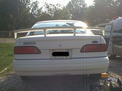 1994 Ford Taurus - The rear of a white sedan is shown with a prominent spoiler and taillights.