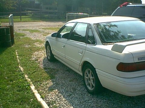1994 Ford Taurus - A white sedan is parked on a gravel lot next to a grassy area.