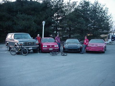 1994 Ford Bronco - A group of people and four vehicles are gathered in a parking lot on an overcast day.