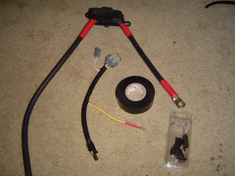 Wiring harness with red-taped battery cables, electrical tape roll and connectors on carpet