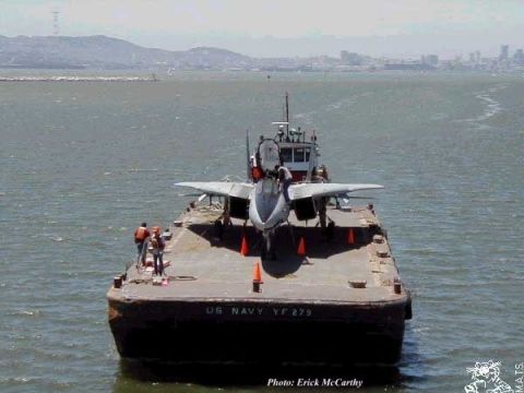 1993 Ford Bronco - A barge labeled 'US NAVY YF 279' transports a fighter jet across the water, with a city skyline in the background.