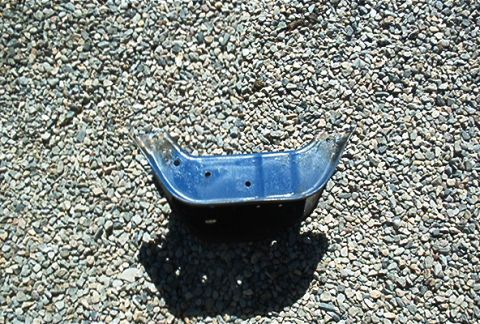 1986 Ford Bronco - A blue metal automotive part rests on a bed of gravel, with a website watermark visible in the lower right corner.