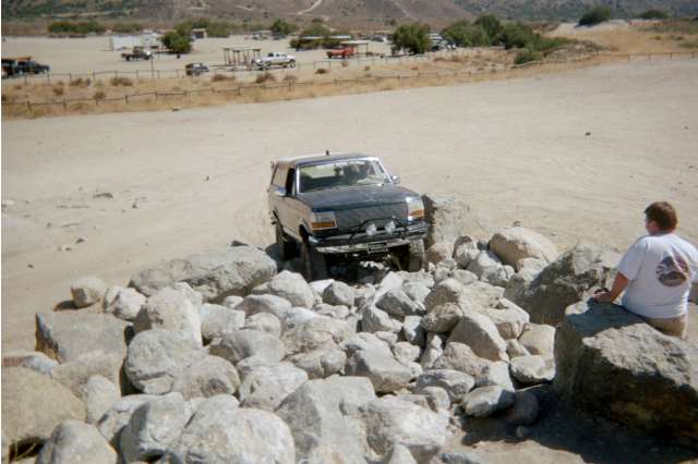 Dark Ford Bronco climbing a boulder pile as a man watches