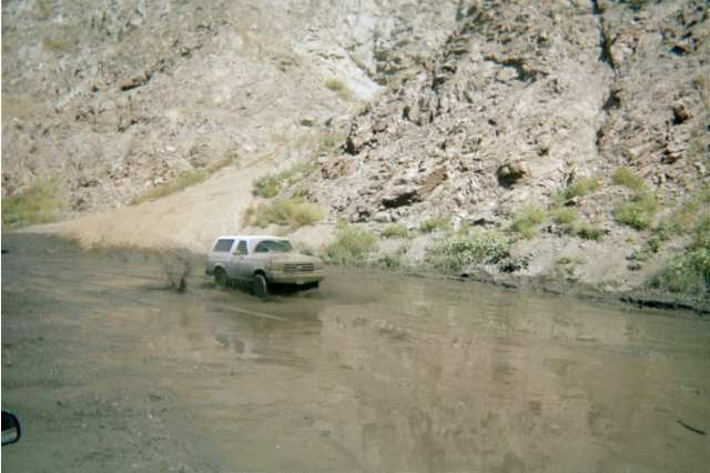 Silver SUV fording muddy water at the base of a rocky canyon wall