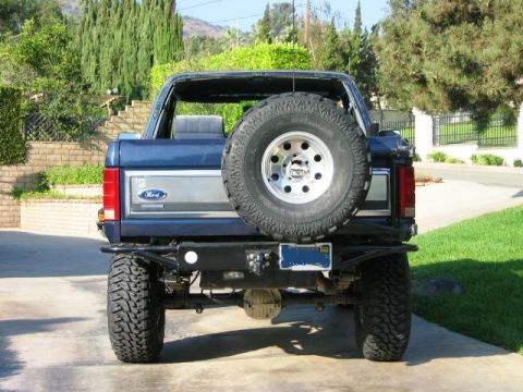 1985 Ford Bronco - Rear view of a blue 1985 Ford Bronco, showing its spare tire and aftermarket bumper.